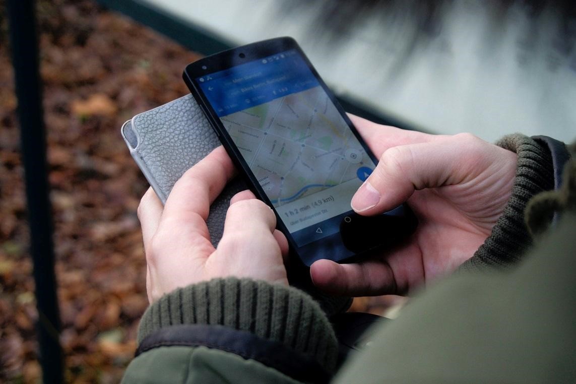 A person in a green jacket using Google Maps on a smartphone for directions.